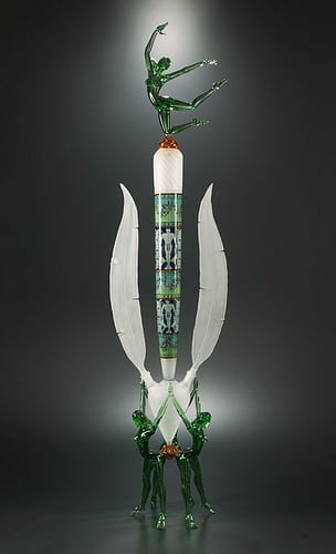 A 42-inch flameworked glass sculpture by Robert Mickelsen: a patterned column flanked by two translucent white wing shapes, a green dancing figure at the top and a cluster of green figures forming the base