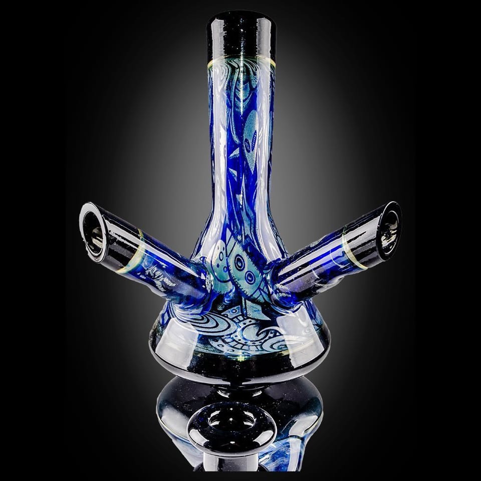 Blue-and-white patterned glass piece by Robert Mickelsen with a tall neck and two horn-shaped mouthpieces, photographed on black
