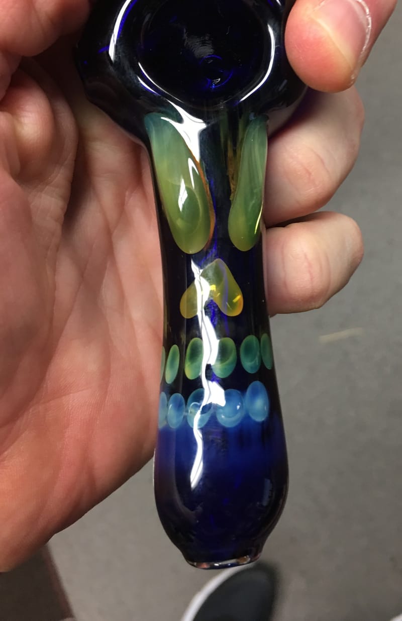 A cobalt blue and green hand-blown spoon pipe held in one hand