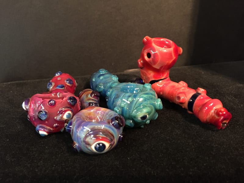 A set of character hand pipes in red, teal and pink, each worked with eyes and small horns