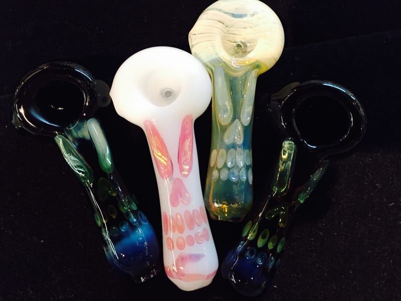 Four hand pipes, one opaque white with pink cane work, photographed on a dark ground
