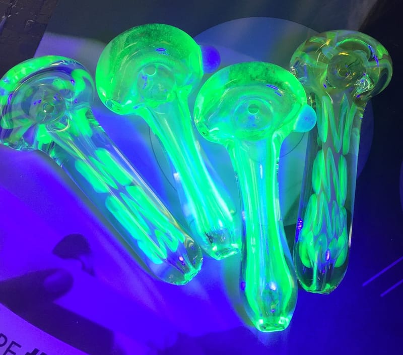 UV-reactive glass hand pipes glowing green under blacklight