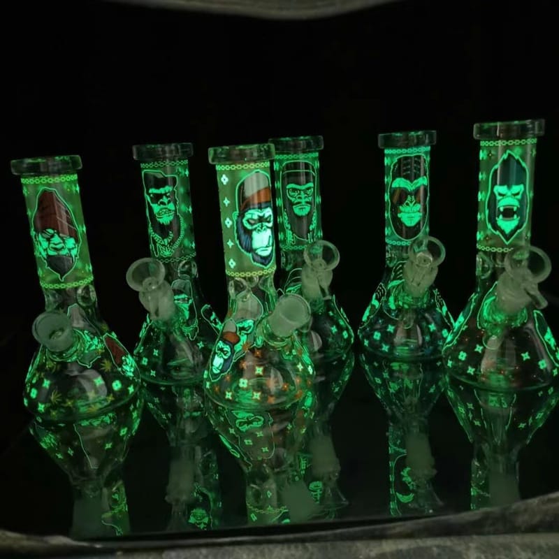 A row of UV-reactive water pipes glowing green under blacklight, each printed with a skull motif