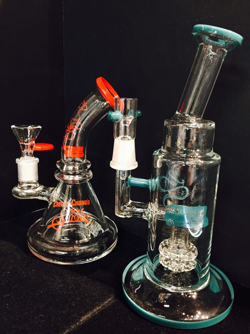A teal and orange dab rig with a recycler arm, beside a clear percolator tube