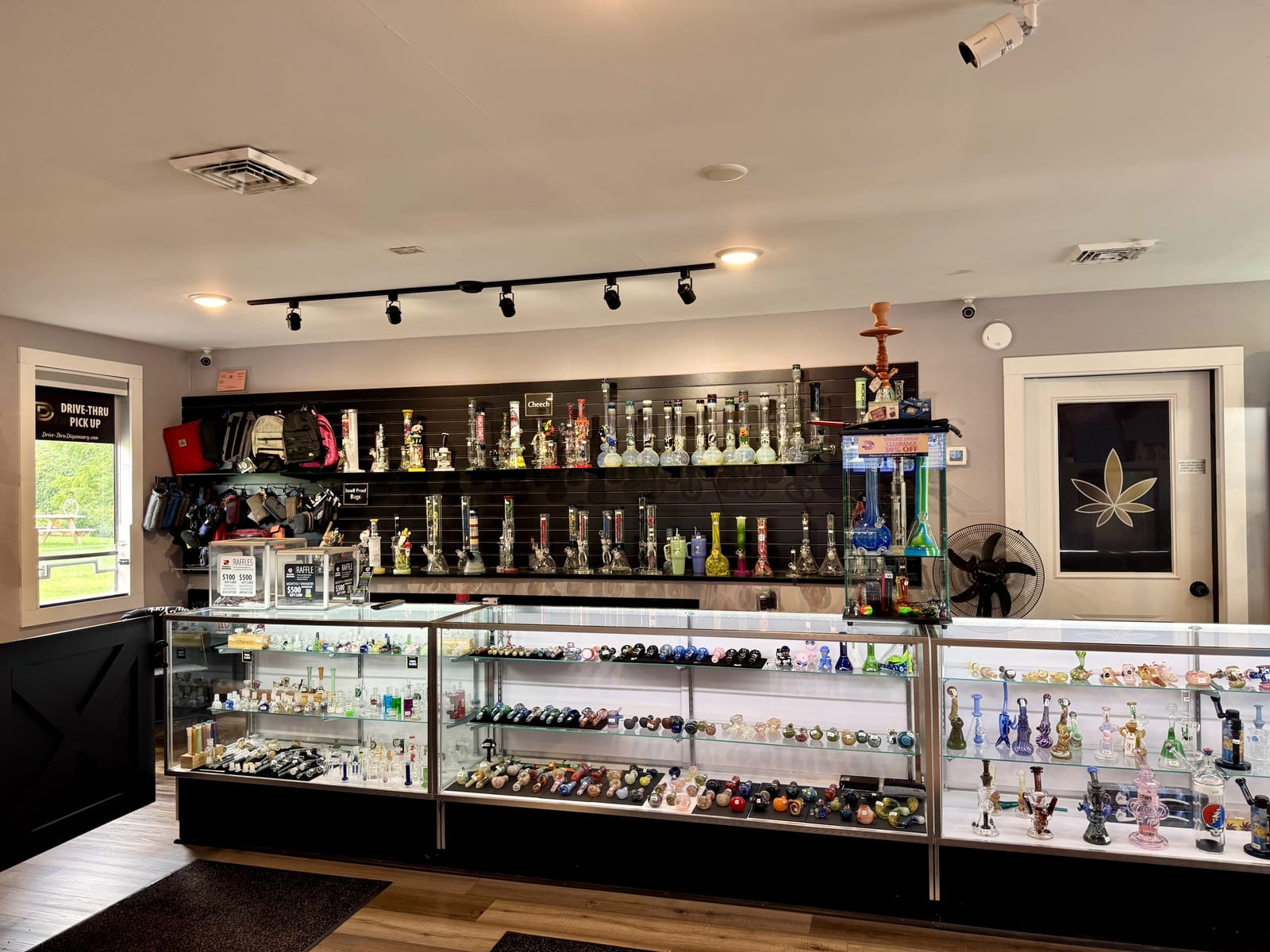 The smoke shop wall at Dryden Dispensary — a long lit case of hand pipes and bubblers, with water pipes ranked along the slatwall behind it and a hookah at the end